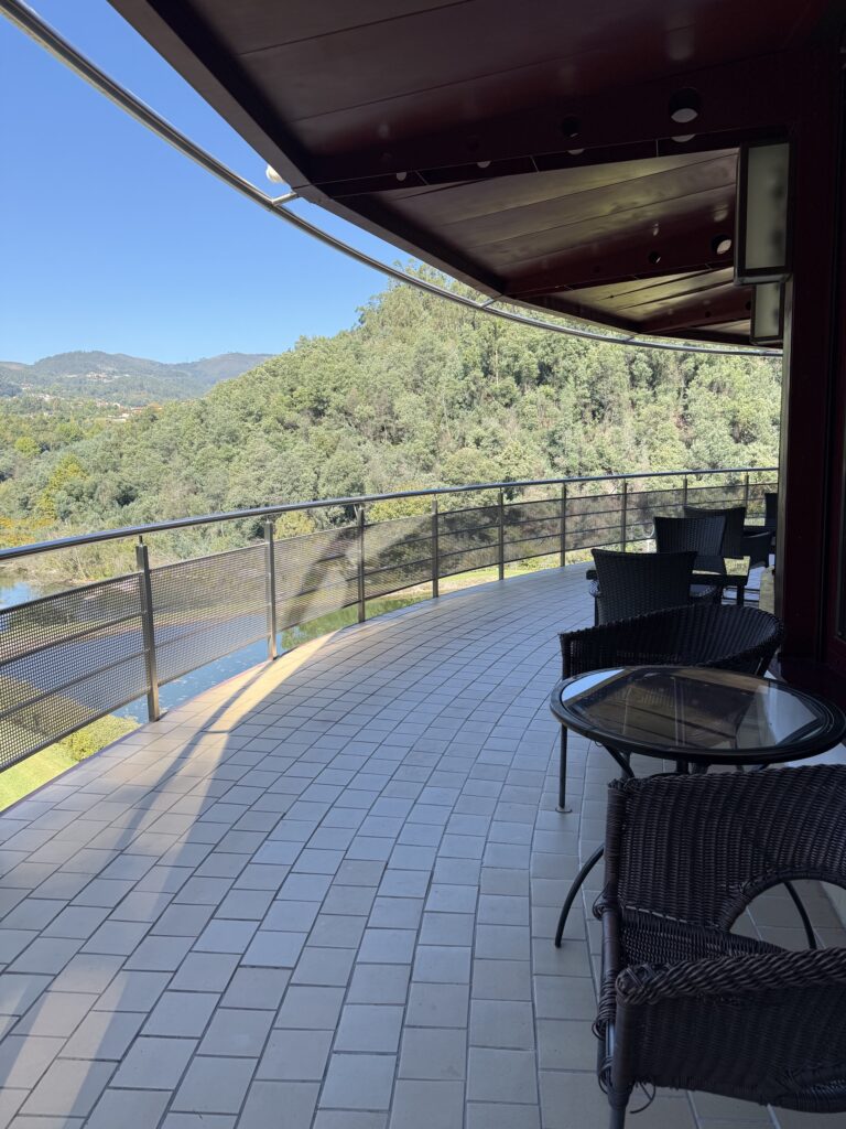 A covered terrace with chairs overlooking wooded hills